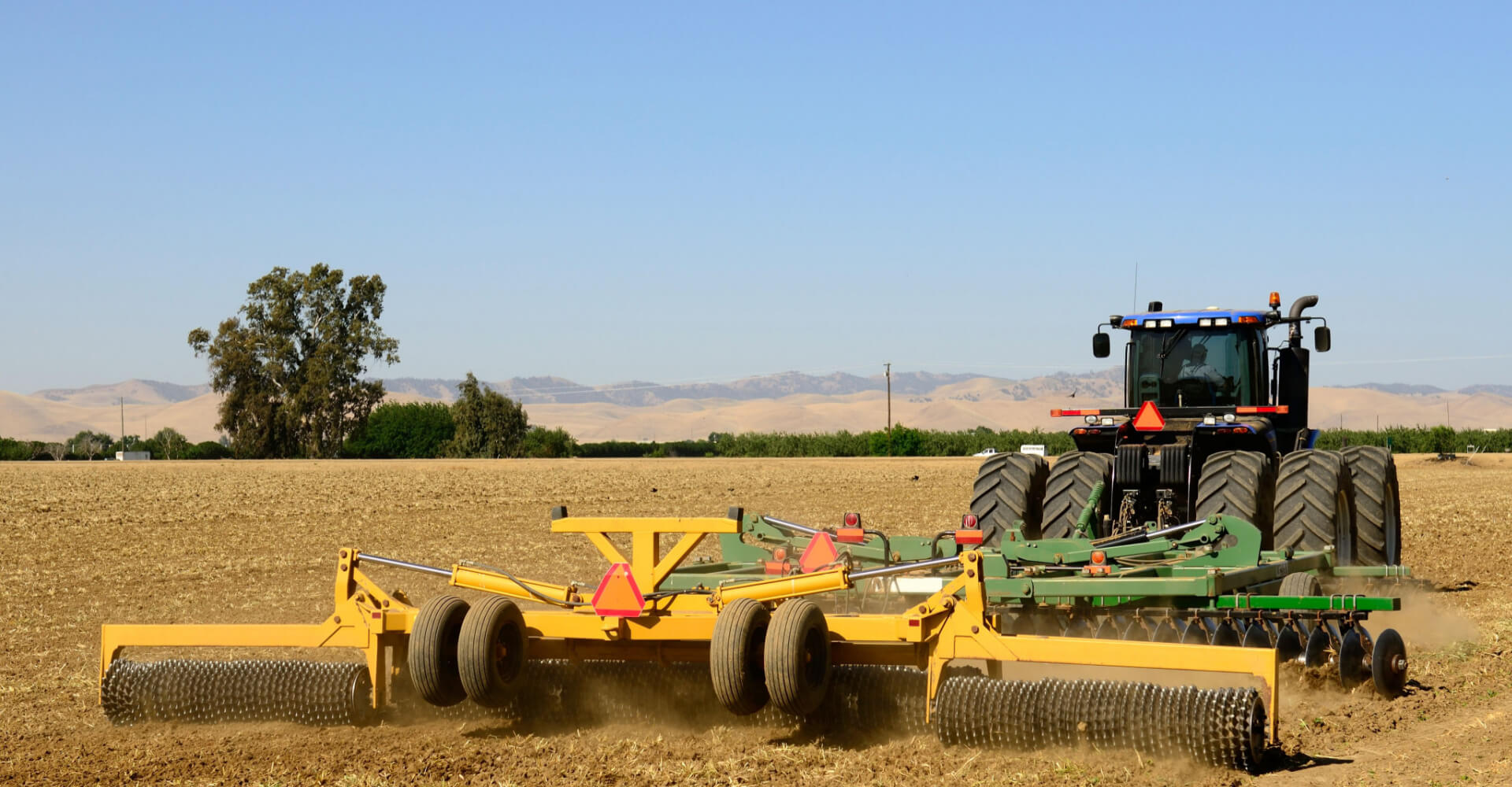 A tractor pulls a disc harrow system implement to smooth over a dirt field in preparation for planting in central California